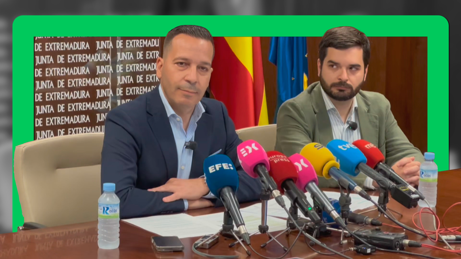 Ángel Pelayo Gordillo e Ignacio Higuero, consejeros de la Junta de Extremadura, en una rueda de prensa con banderas de España y Extremadura de fondo. Se aprecian micrófonos de EFE, Europa Press, TV y RNE.