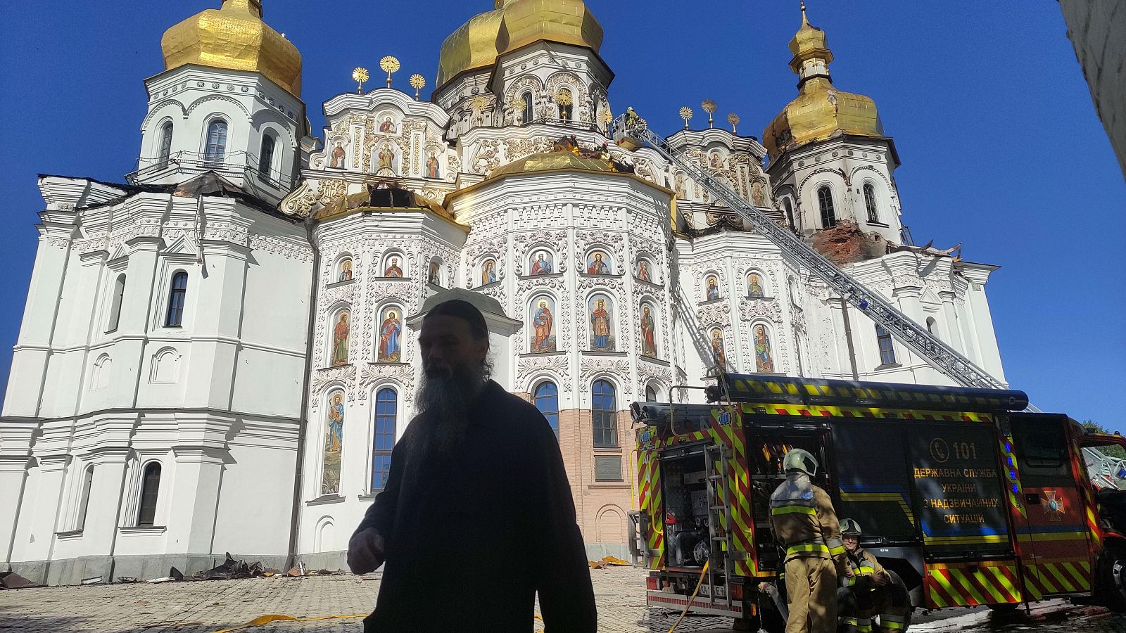 Catedral de la Dormición de Kiev dañada, con bomberos y un camión de emergencias (Servicio Estatal de Emergencias de Ucrania, número 101) actuando. Un monje observa la escena.