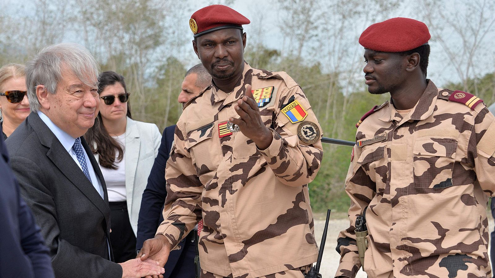 António Guterres, Secretario General de la ONU, saluda a soldados chadianos en un encuentro al aire libre. El soldado central viste uniforme de camuflaje y boina roja con la bandera de Chad.
