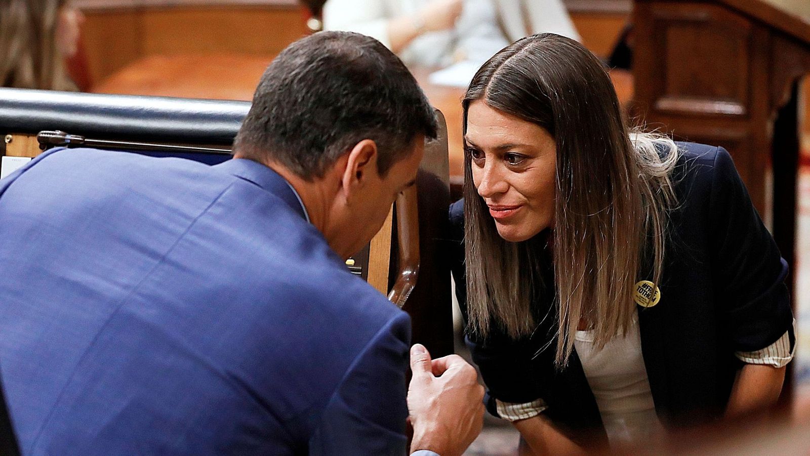 Pedro Sánchez y Míriam Nogueras conversan íntimamente en el Congreso. Sánchez viste traje azul oscuro, Nogueras americana azul marino con mangas remangadas y un pin dorado en la solapa.