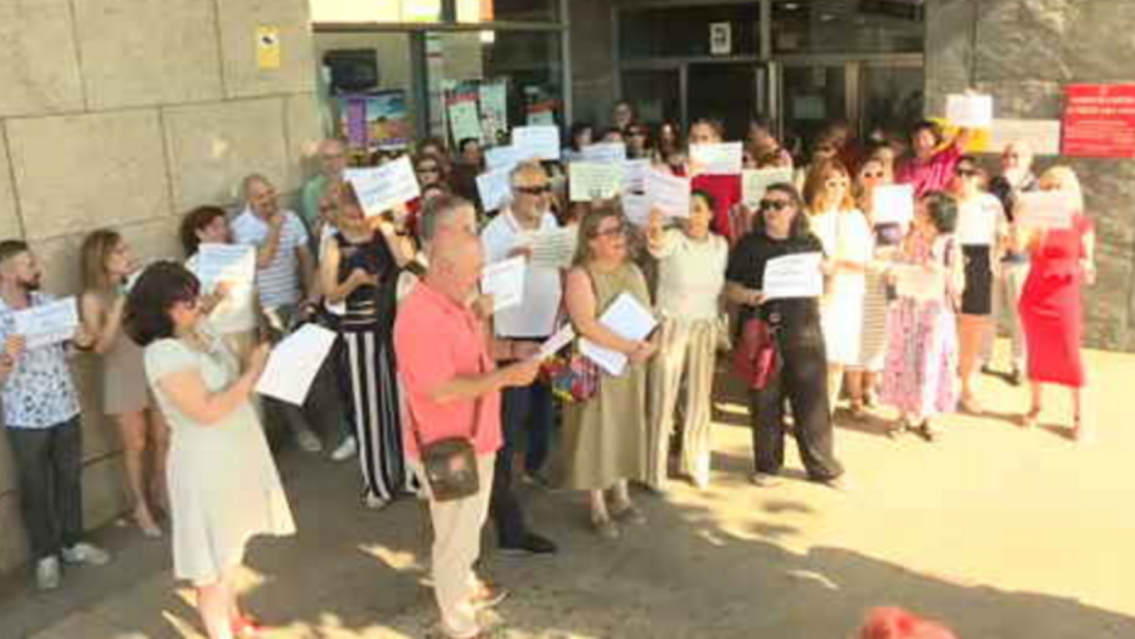 Manifestación de funcionarios ante los Juzgados de Cáceres. Un hombre con gafas de sol y camisa salmón dirige al grupo que porta carteles.