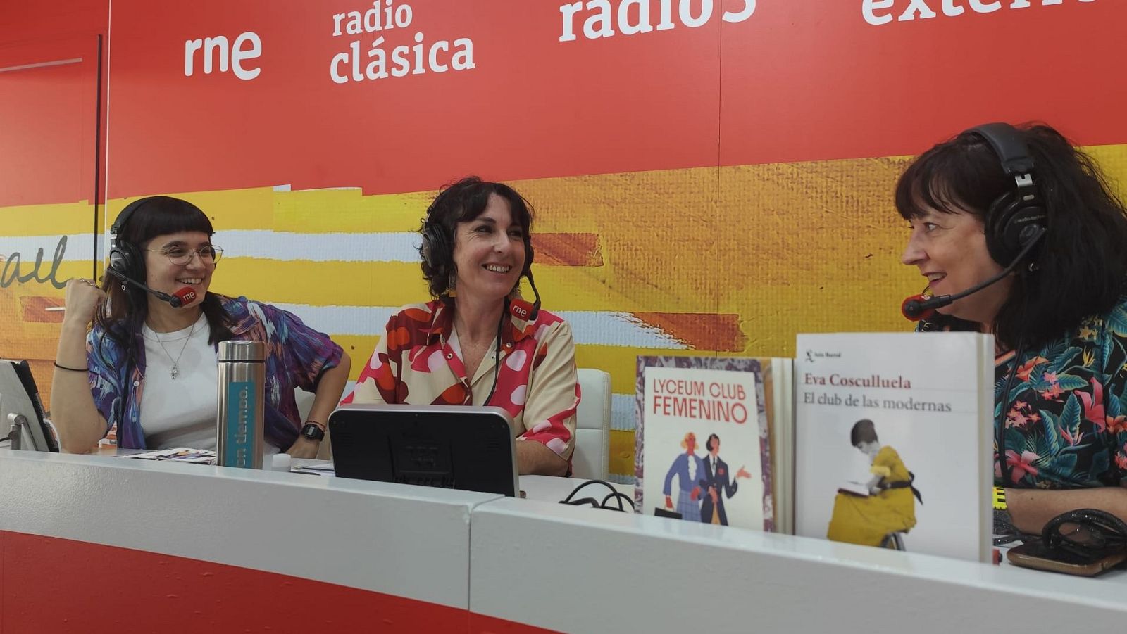 Rocío Elorrieta, Lola Martínez Rojo y Eva Cosculluela en una emisión de radio con auriculares, rodeadas de libros y logotipos de RNE.