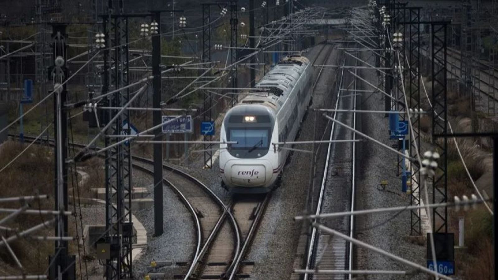 Tren d'alta velocitat blanc de Renfe en una xarxa de vies amb catenària i senyals. Es veu el logotip 'renfe' i senyals amb 'Canton un' i '60m'.