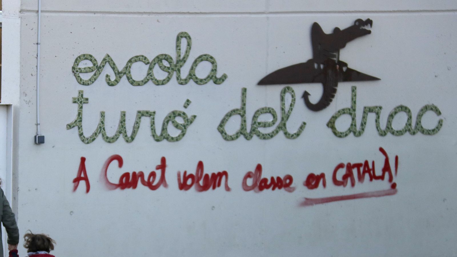 Fachada de l'escola Turó del Drac amb pintada "A Canet volem classe en CATALÀ!" en vermell, nom de l'escola en verd i logotip de drac.
