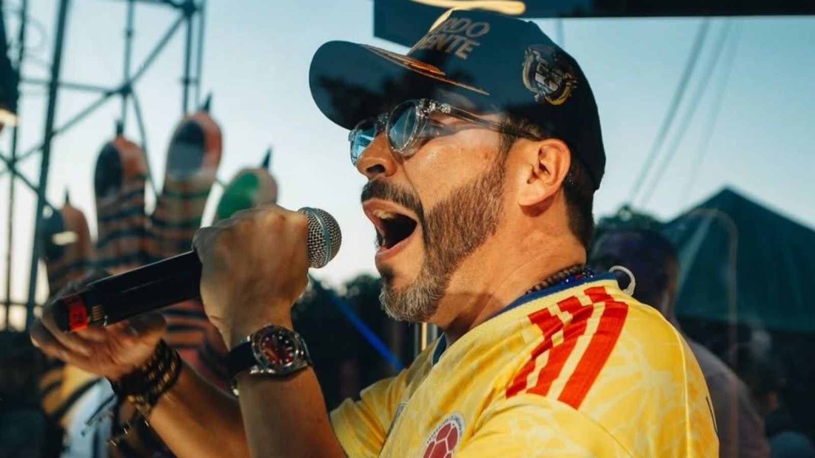 Primer plano de Abelardo de la Espriella, candidato presidencial colombiano, con expresión intensa, boca abierta, vistiendo camiseta de fútbol de Colombia, gafas de sol y gorra.