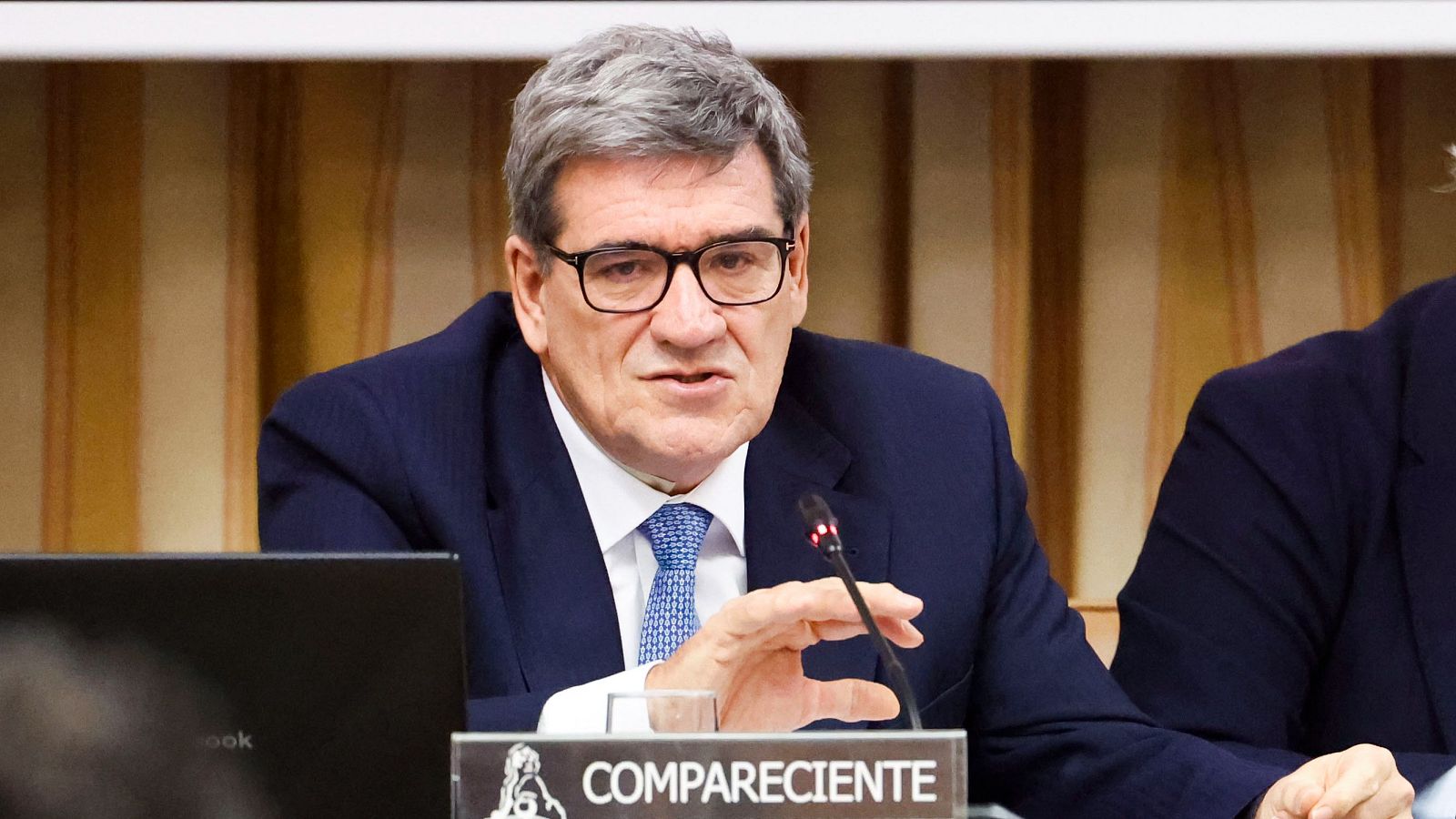 José Luis Escrivá, gobernador del Banco de España, comparece ante la Comisión de Economía del Congreso, hablando ante un micrófono con un cartel de "COMPARECIENTE".