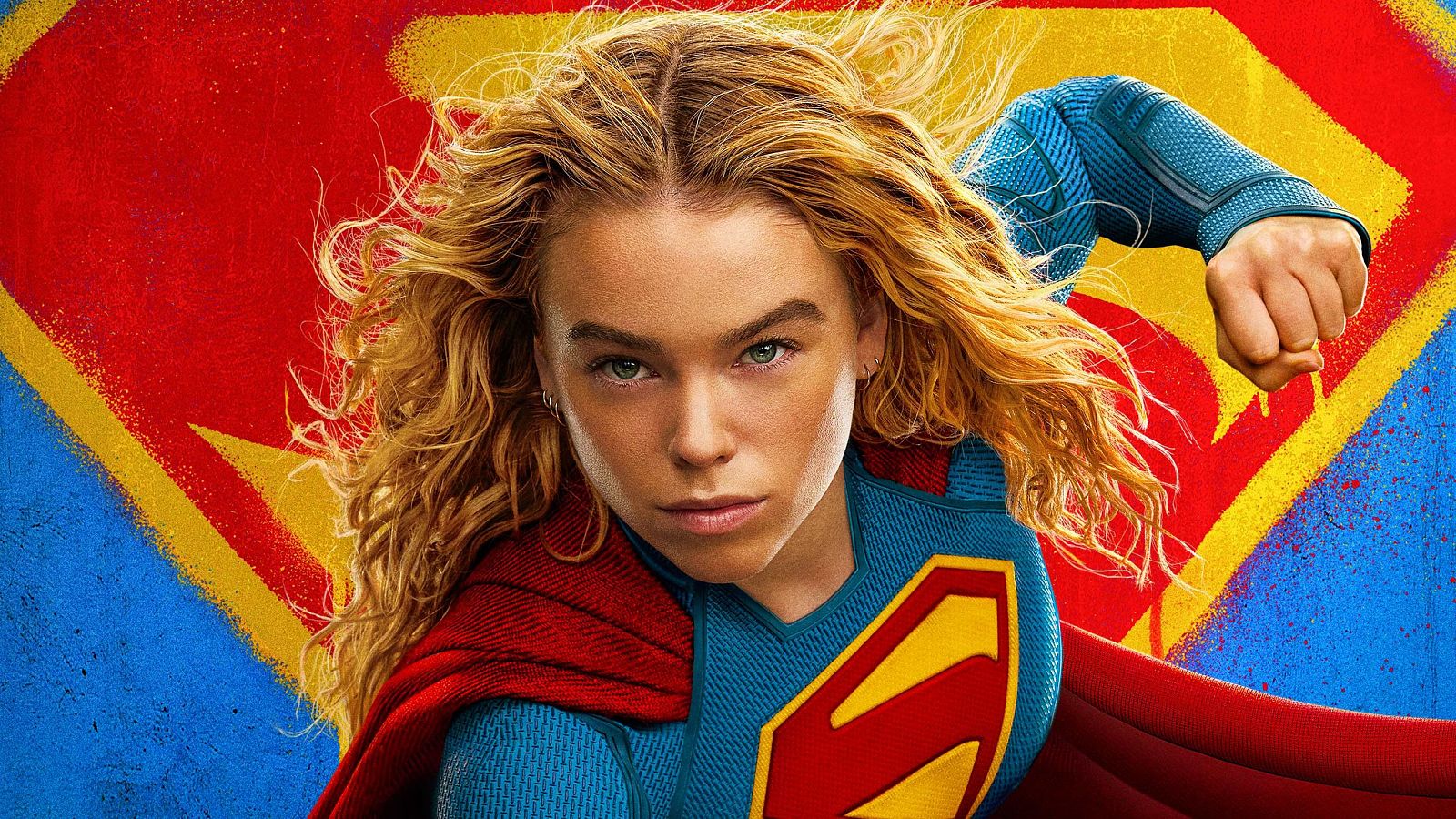 Milly Alcock como Supergirl, con traje azul, capa roja y emblema 'S'. Fondo de grafiti del emblema 'S'.
