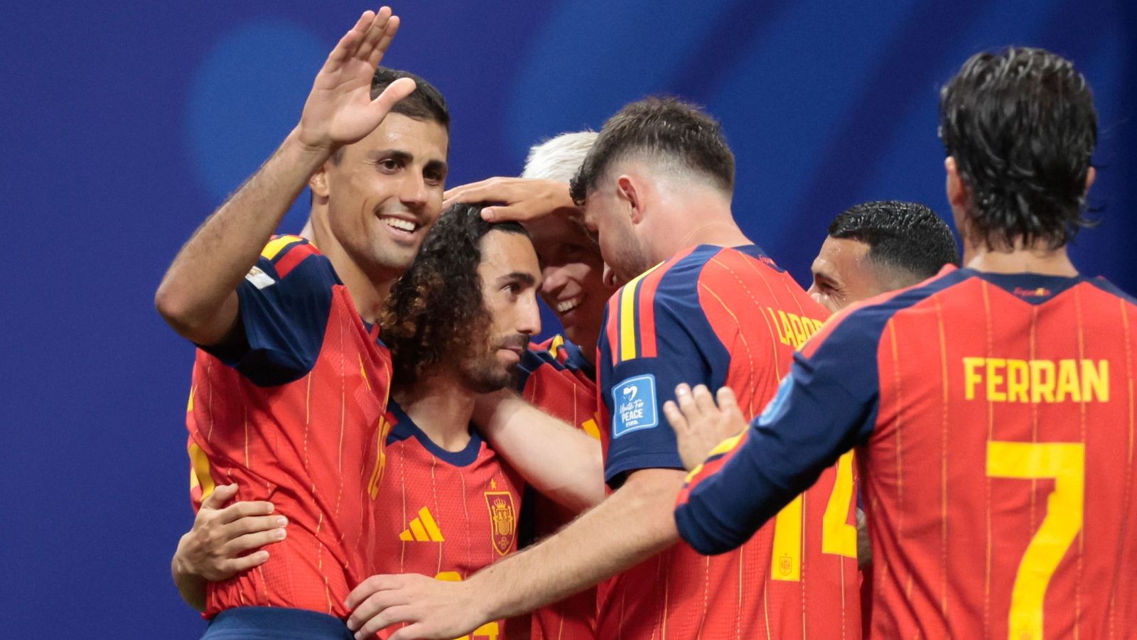 Jugadores de la selección española celebran un gol. Se ven a Busquets, Cucurella y Ferran Torres (con dorsal 7) con la equipación roja y detalles amarillos y azules.