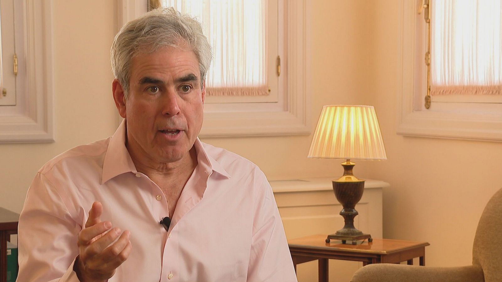 Psicólogo social Jonathan Haidt, de frente, con camisa rosa y mano levantada, en una habitación con ventana y lámpara.