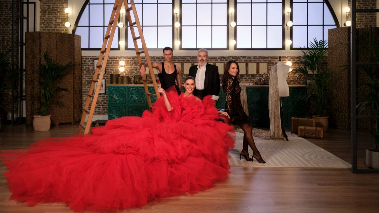 Raquel Sánchez Silva, Luis de Javier, Lorenzo Caprile y María Escoté posan en un plató con estética industrial. Raquel luce un vestido rojo, Luis un top negro, Lorenzo un traje oscuro y María un vestido de encaje.