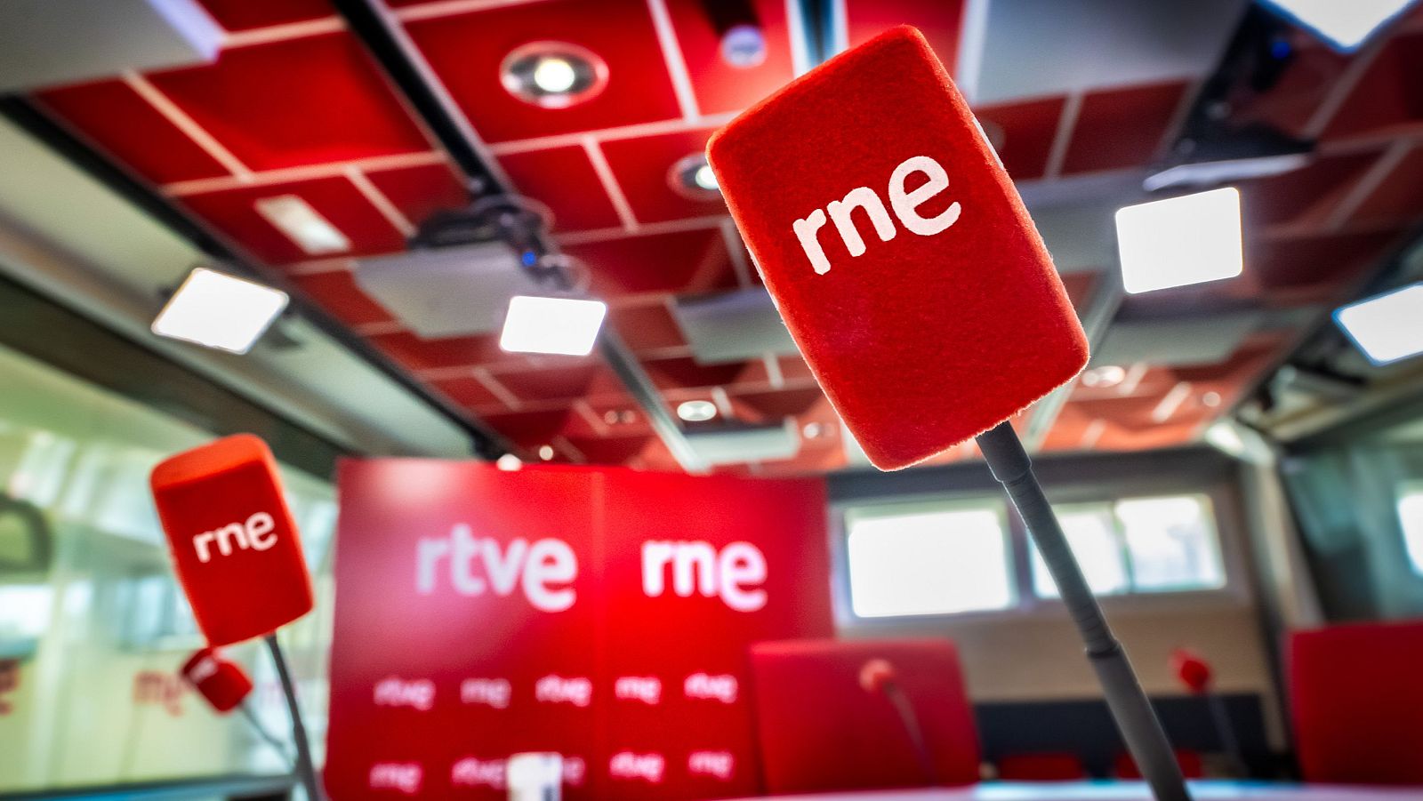 Set de radio/TV en rojo y blanco con micrófonos "rne" y logo "rtve rne" en el fondo. Sin personas.