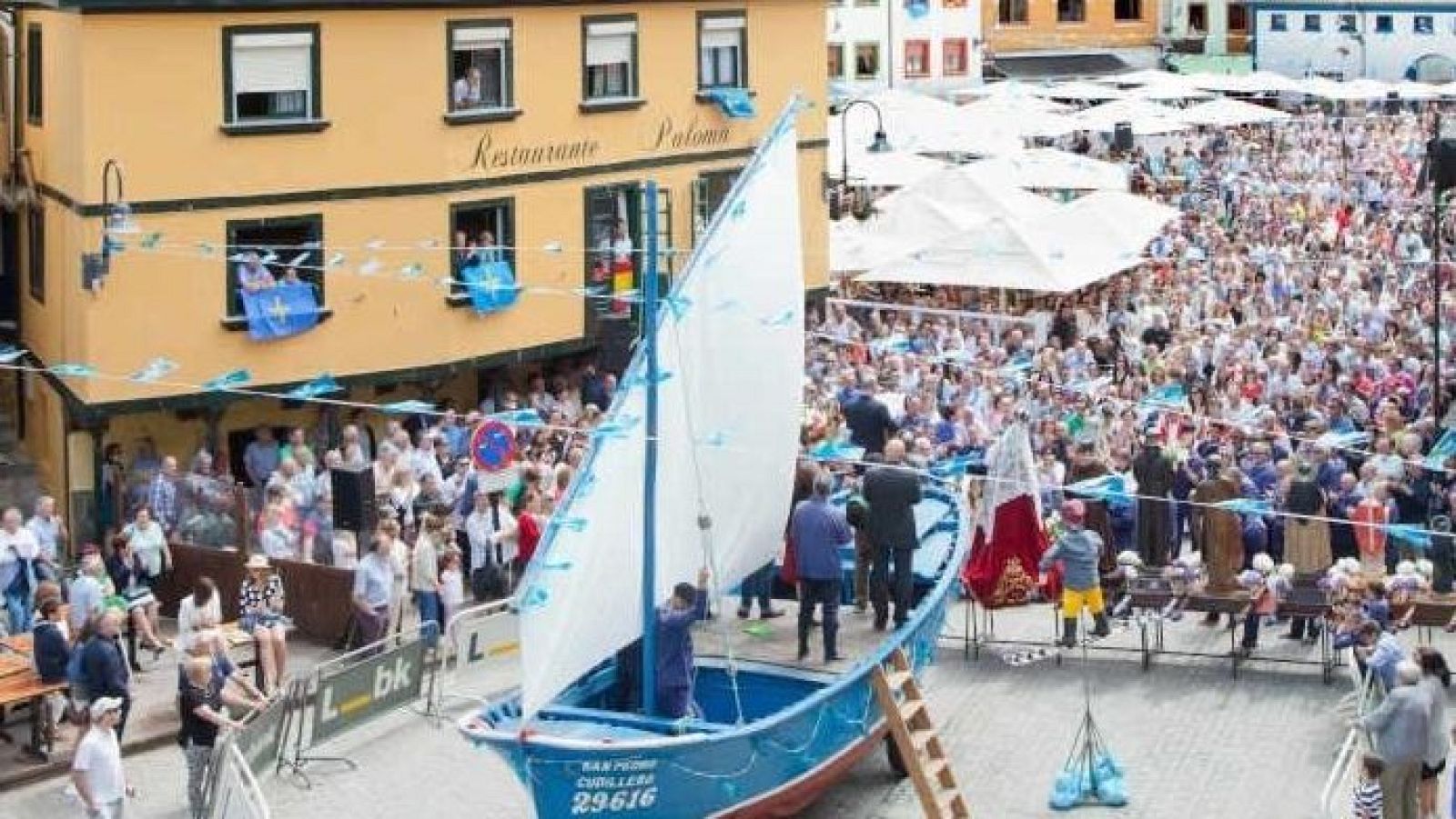 Festividad de L'Amuravela en Cudillero: barco "SAN PEDRO CUDILLERO 29616", procesión religiosa, multitud y banderas asturianas.