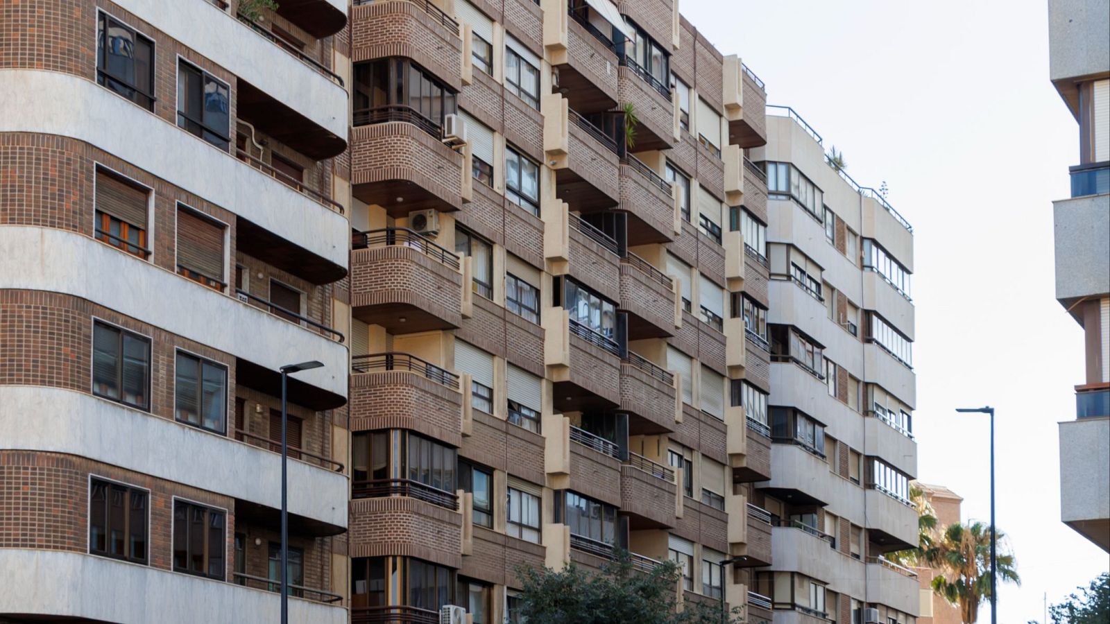 Vista frontal de edificios residenciales urbanos con fachadas de ladrillo y balcones. Se aprecian ventanas con persianas y elementos arquitectónicos variados.