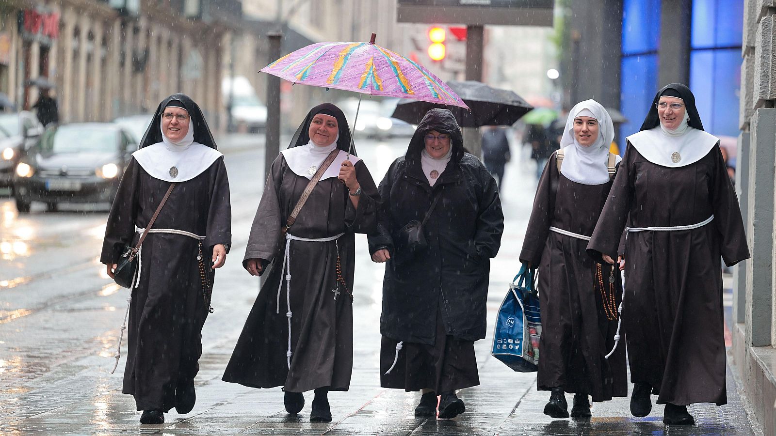 Cinco exmonjas de Belorado caminan en fila por una calle urbana mojada bajo la lluvia, dirigiéndose a una comparecencia judicial el 4 de mayo de 2025.