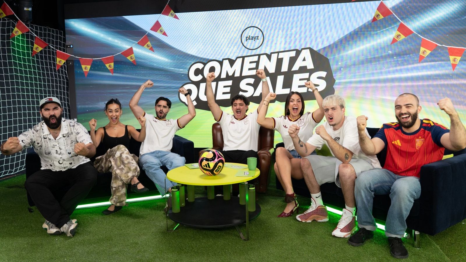 Siete figuras digitales, entre ellas Ibai Llanos y DjMaRiiO, celebran con júbilo en un plató deportivo con temática de fútbol, luciendo la bandera española y el logo "playz".