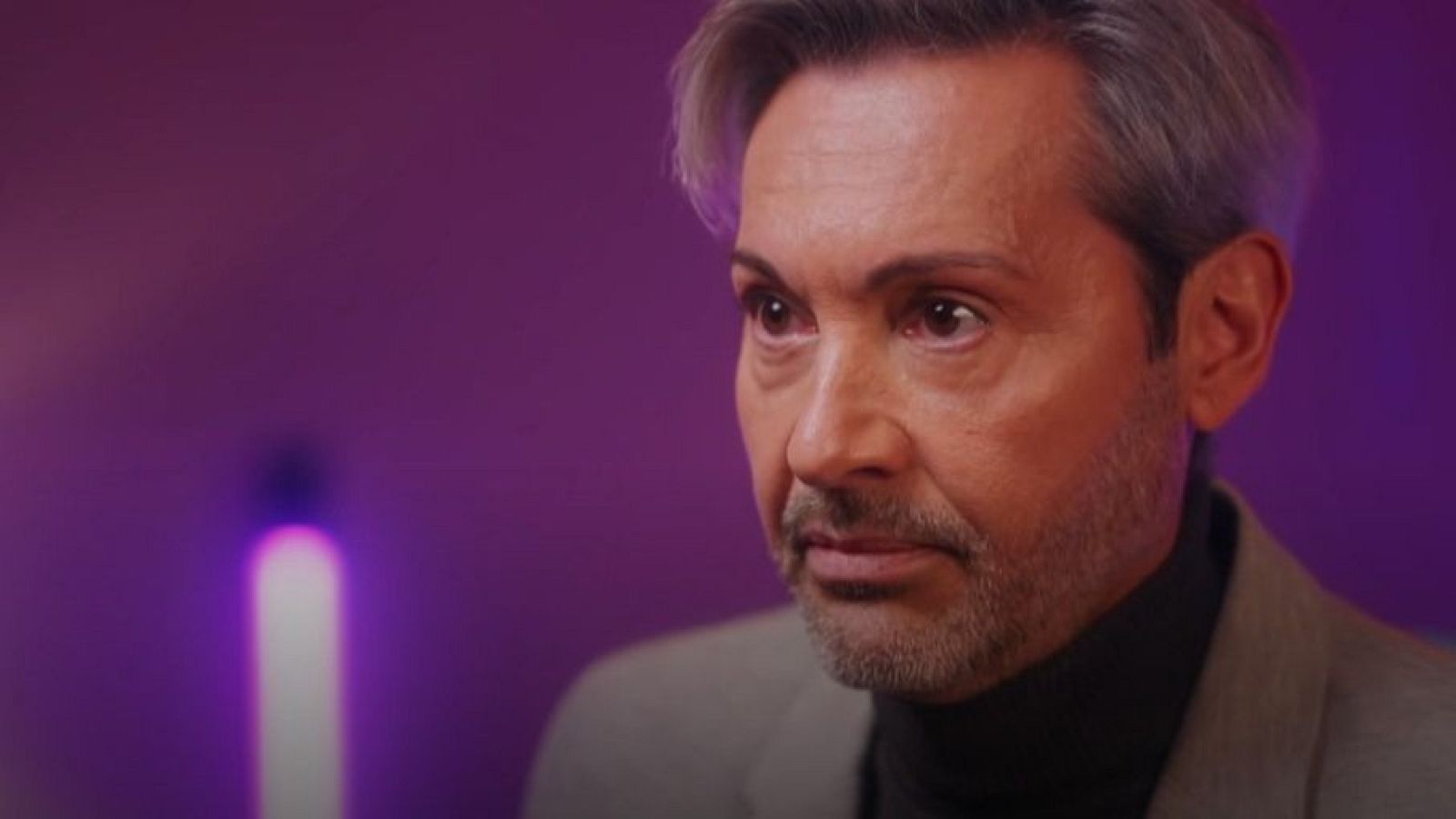 Manuel Arjona, hombre de mediana edad con cabello y barba canosos, viste traje gris y jersey negro. Expresión seria, mirada reflexiva.