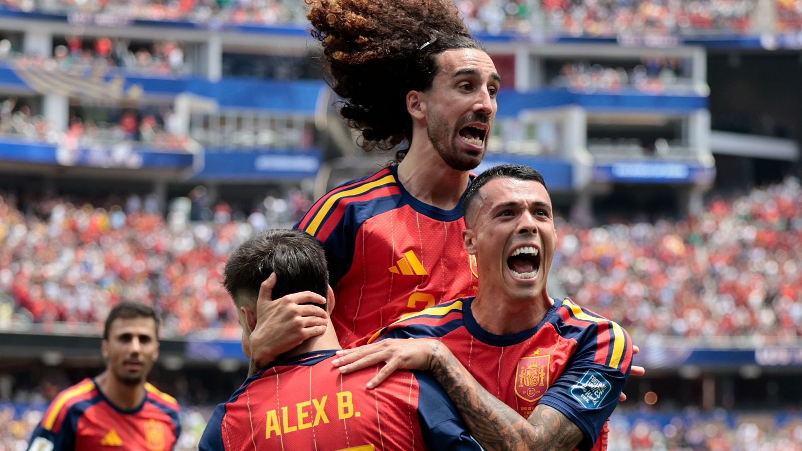 Futbolistas españoles celebran un gol en un estadio lleno. Se distinguen Lucas Vázquez, Marc Cucurella, Álex Baena y Dani Carvajal. La afición viste de rojo y blanco.