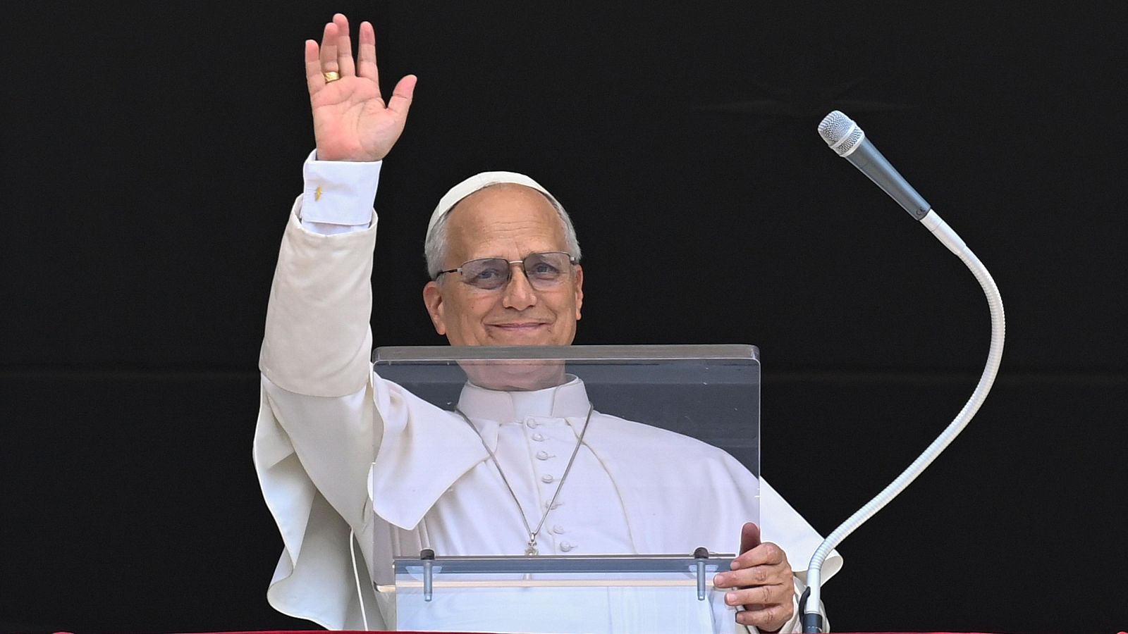 El Papa Francisco saluda con una sonrisa desde el Palacio Apostólico del Vaticano, vestido con atuendo papal y con un micrófono.