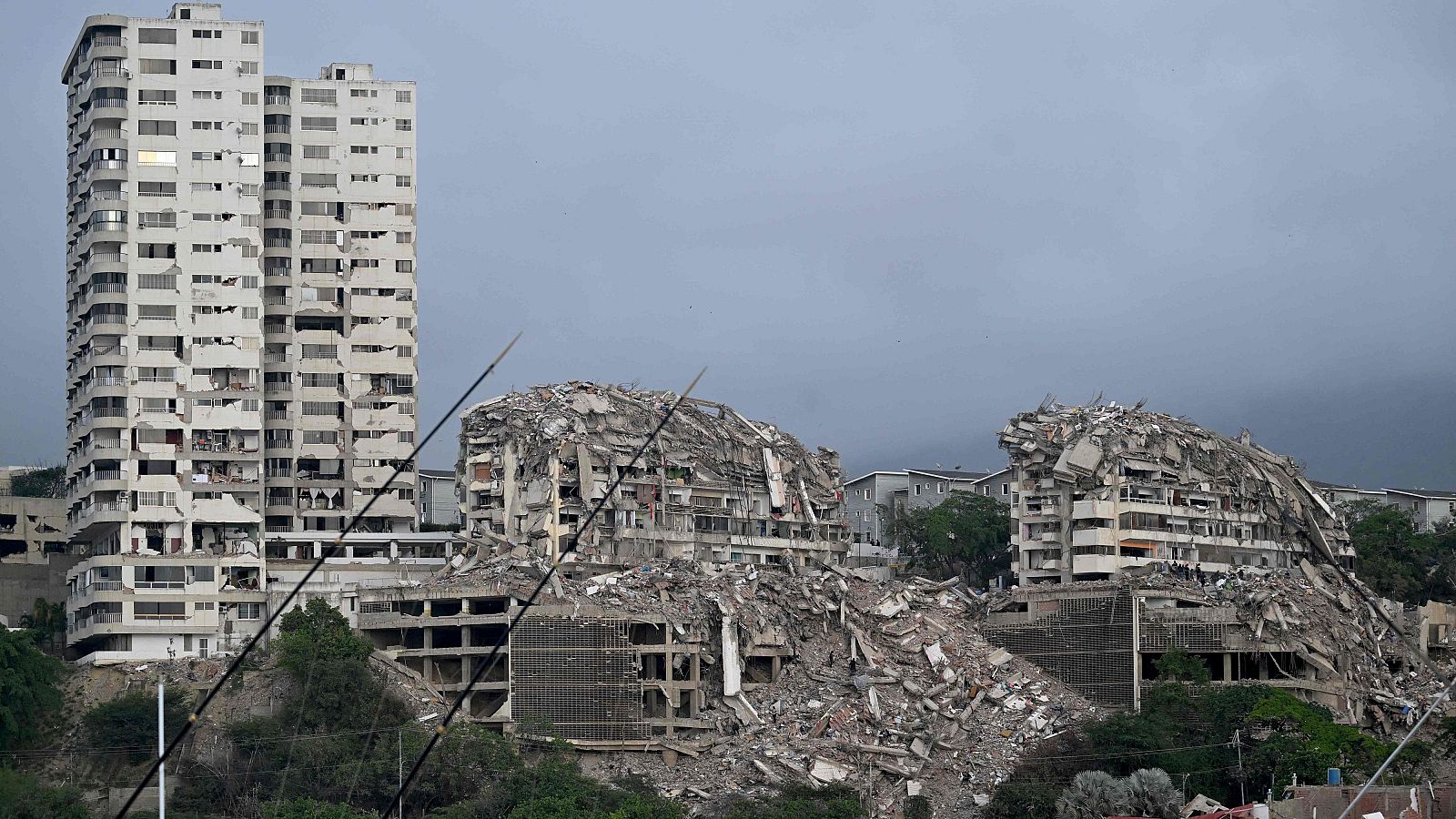Edificios derrumbados y escombros masivos en una zona urbana bajo un cielo gris, evidenciando la devastación de un desastre natural.