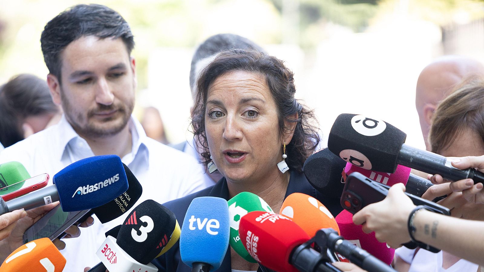 Alicia Romero, consellera d'Economia, davant d'una allau de micròfons de diversos mitjans com Atlasnews, TVE, Europa Press i 3cat, parlant amb una expressió concentrada.