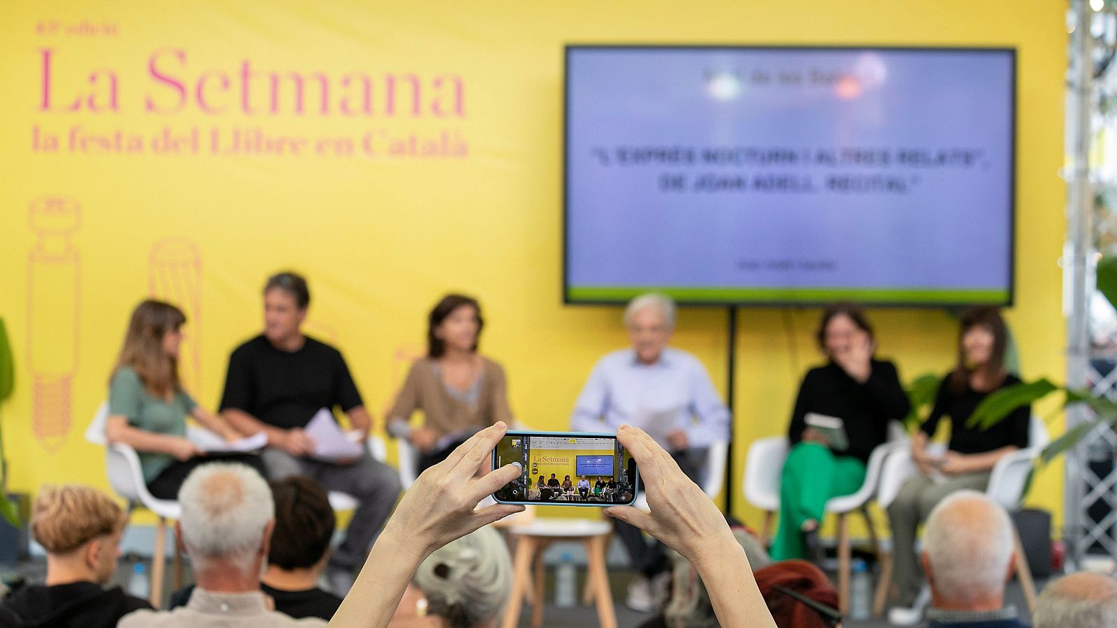 Panell de discussió a la 41a edició de "La Setmana, la festa del Llibre en Català", amb cinc ponents i una pantalla que mostra "L'EXPRESSIÓ NOCTURNA I L'ALTRE RELAT".