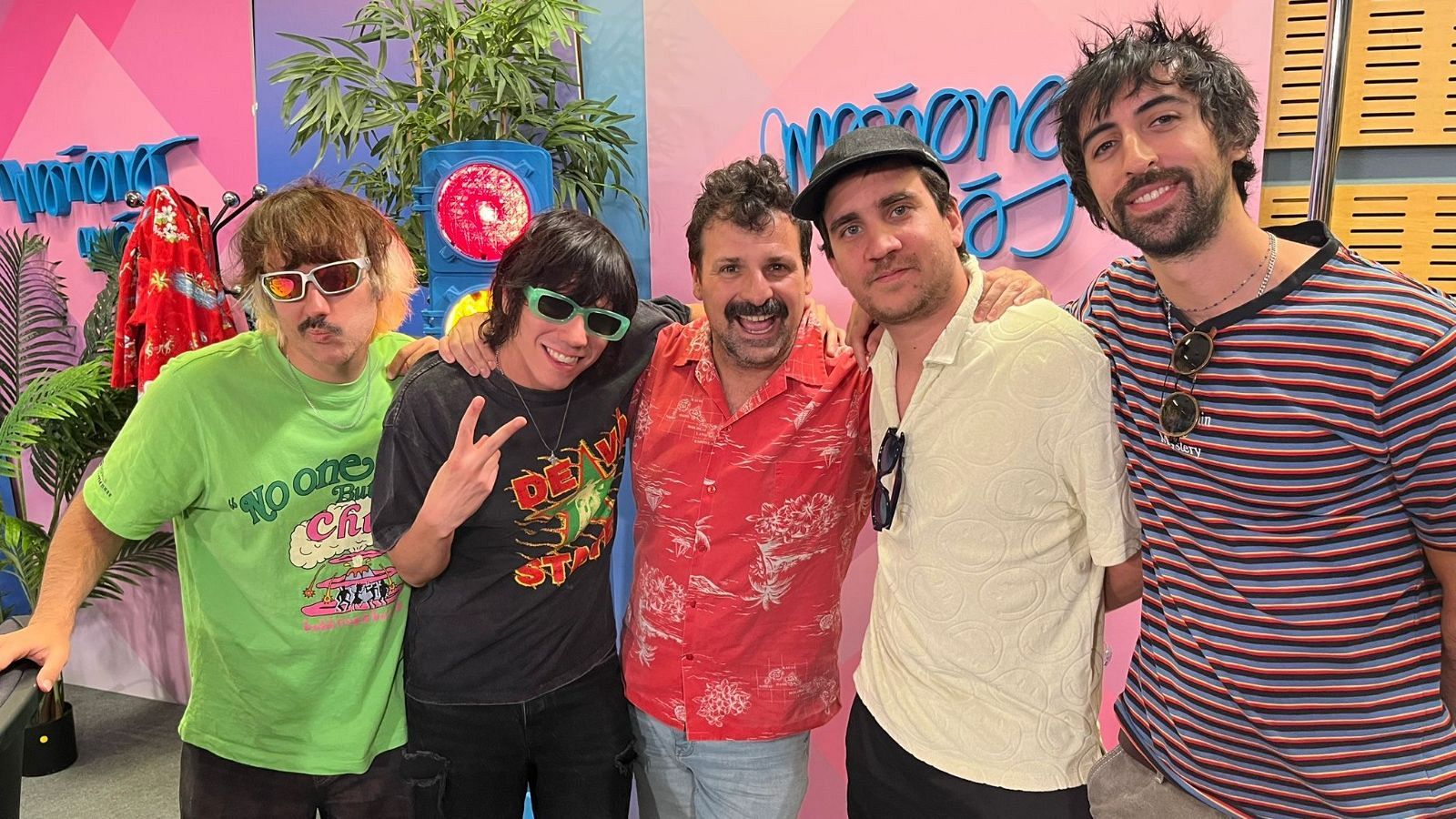 Los cinco integrantes de la banda Cupido posan sonrientes en un set con decoración tropical y un letrero "Mañaneros", probablemente en un programa de RNE.