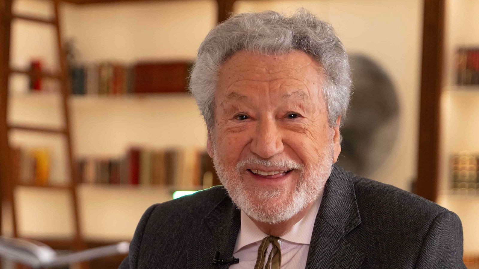 Luis del Val, periodista y escritor, sonríe a la cámara con su característico cabello canoso y barba blanca, vestido con traje gris y camisa clara.