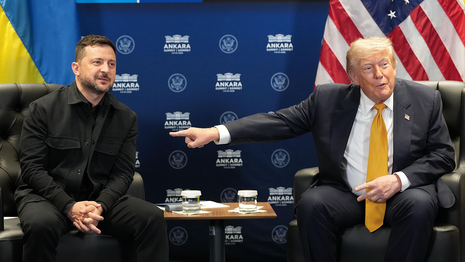 Donald Trump y Volodímir Zelenski en la "ANKARA SUMMIT 2019", con banderas de EE.UU. y Ucrania de fondo. Trump gesticula mientras Zelenski escucha.