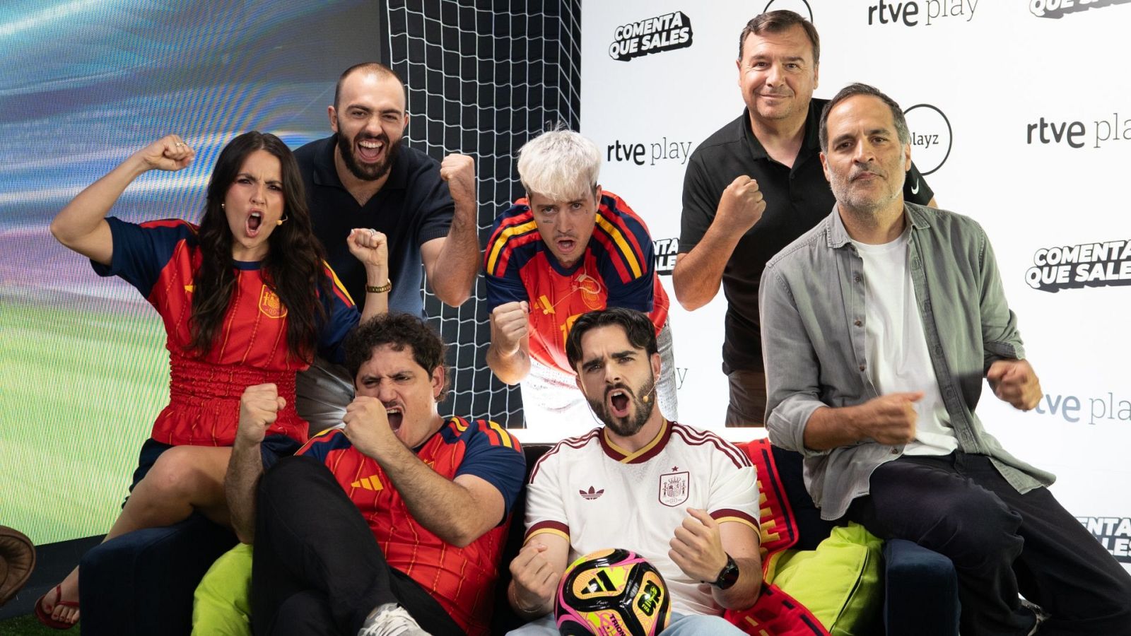 Siete figuras públicas, incluyendo a Ibai Llanos y Cristinini, celebran con euforia en un plató de "rtve play" y "COMENTA QUE SALES", vistiendo camisetas de la selección española y mostrando su pasión por el fútbol.