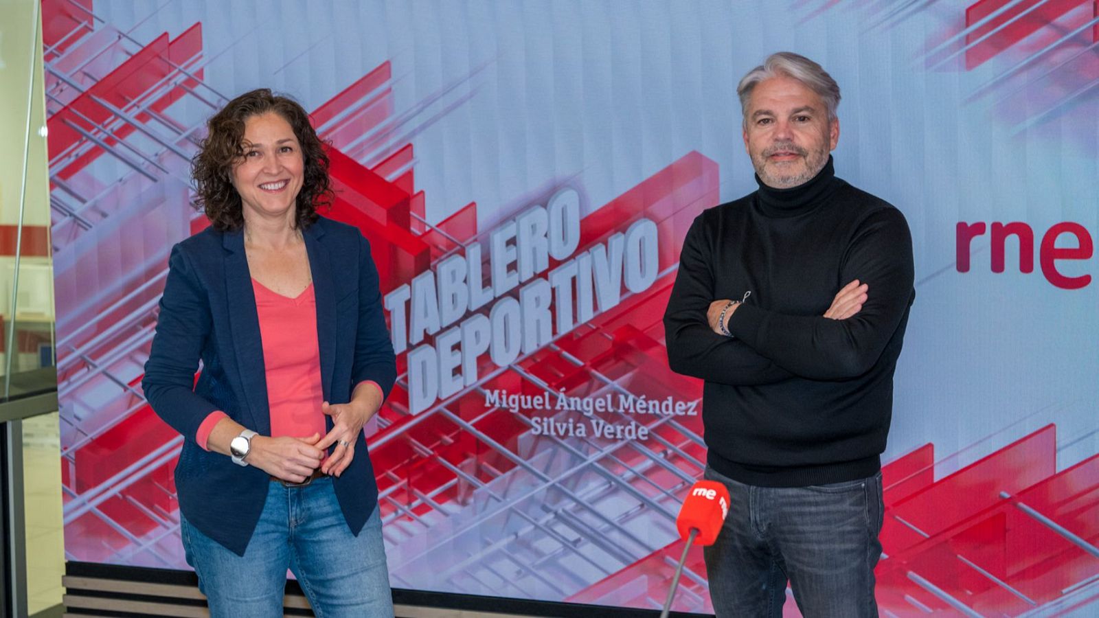 Silvia Verde y Miguel Ángel Méndez, presentadores de "Tablero Deportivo" de RNE, posan sonrientes frente al logo del programa y de la emisora.