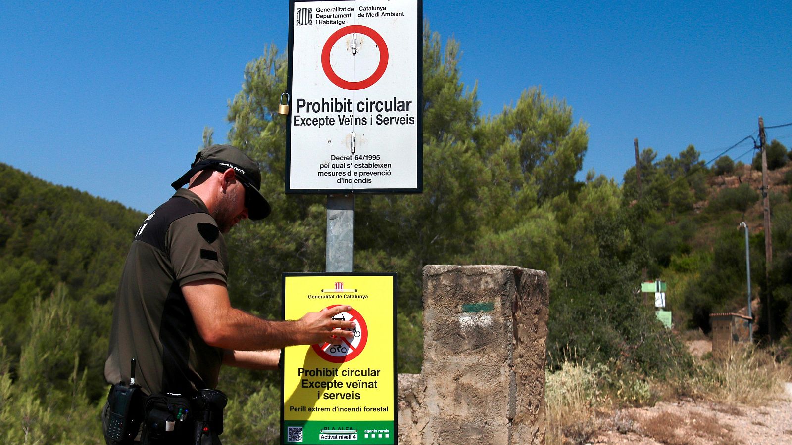 Agente rural ajusta señal de prohibición de circulación en camino forestal, advirtiendo de peligro extremo de incendio forestal y nivel 3 activado.