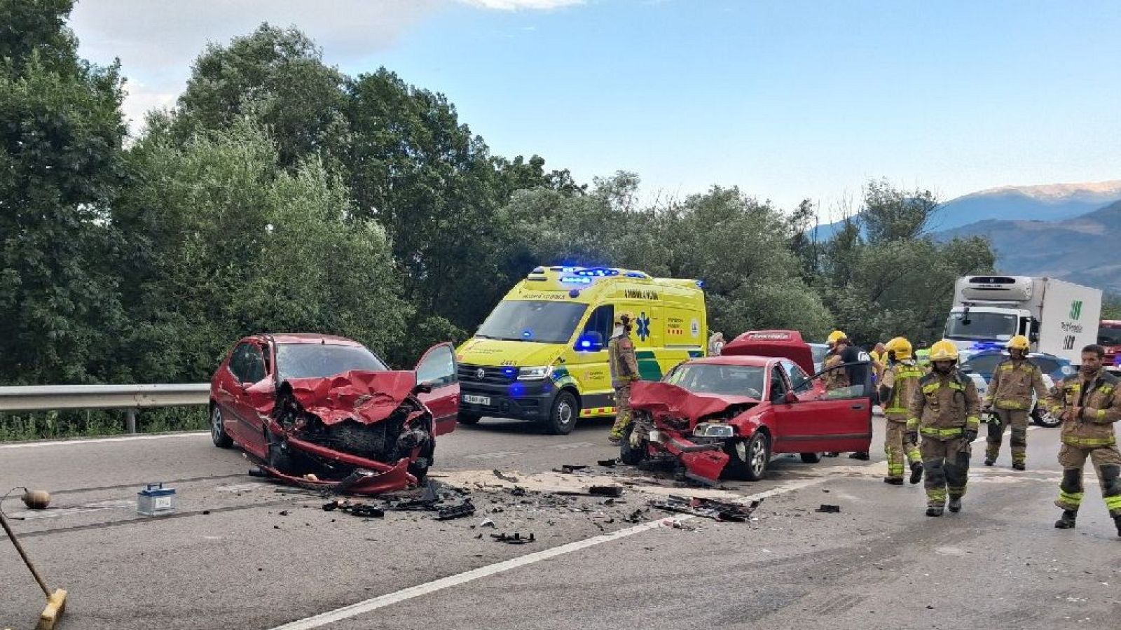 Accidente de tráfico en carretera montañosa con dos coches rojos implicados. Intervienen bomberos y ambulancia de "Emergències Mèdiques".