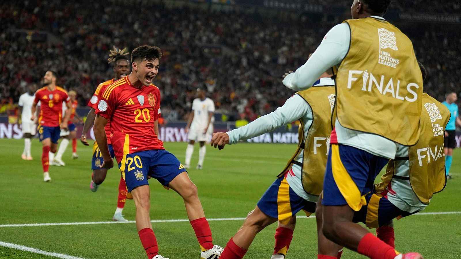 Pedri celebra un gol en la UEFA Nations League Finals, con el dorsal "20" en su camiseta de España, rodeado de compañeros y personal de la UEFA en un estadio abarrotado.