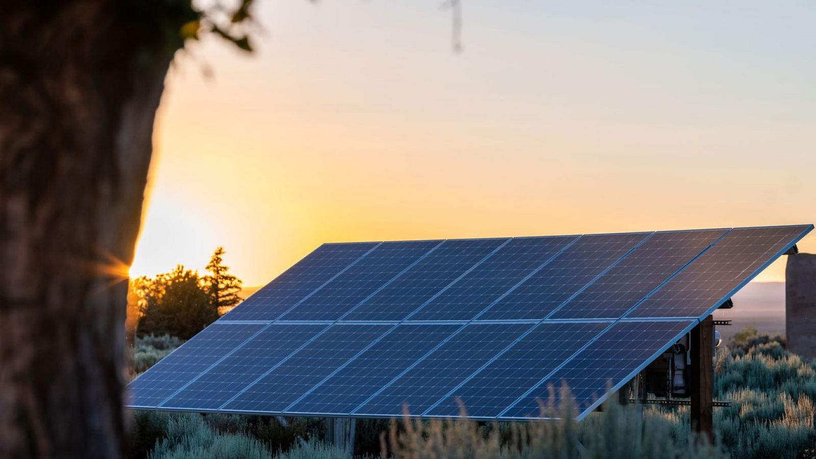 Paneles solares al atardecer, iluminados por el sol poniente.  Instalación en entorno natural con vegetación, representando comunidades solares.