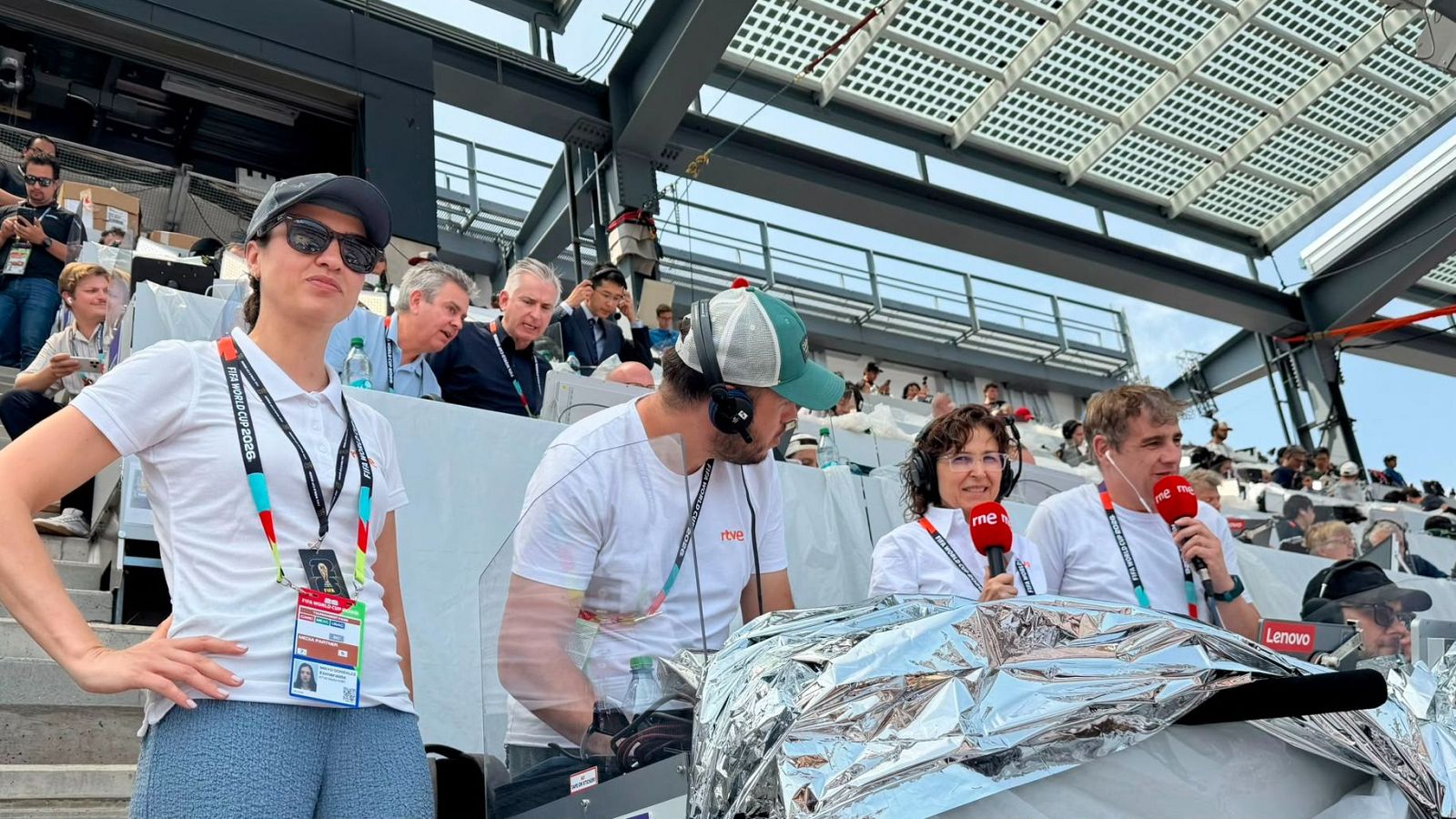 Cuatro miembros del equipo de RNE, incluyendo a Sara Tabares y Antonio Muelas, cubren un evento deportivo desde un palco de prensa con micrófonos y equipo de retransmisión.