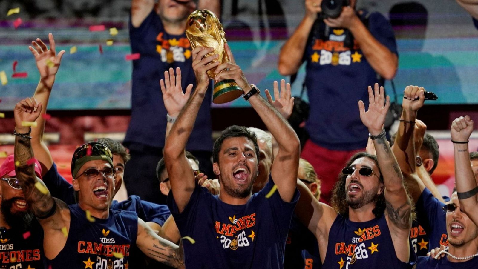 Rodri, Pedro Porro y Marc Cucurella celebran con la Copa del Mundo y confeti, luciendo camisetas de "CAMPEONES 20 26".