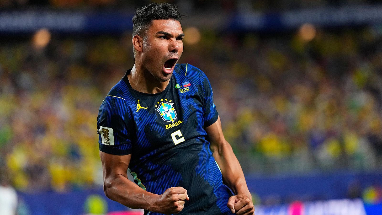 Casemiro, futbolista brasileño, celebra con euforia vistiendo la camiseta de Brasil con el escudo de la CBF y el logo de Jordan. Fondo de estadio desenfocado.