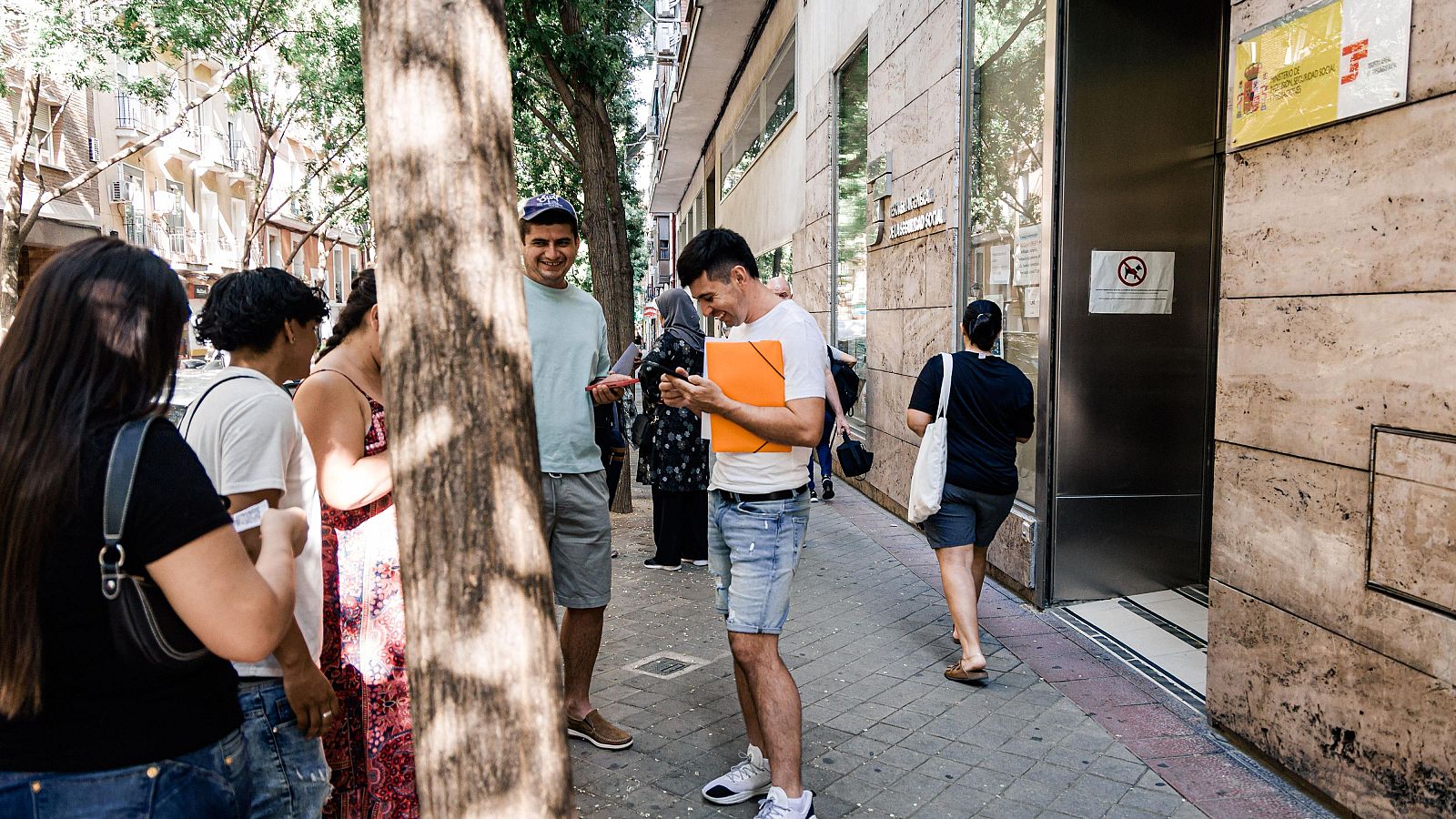 Varias personas migrantes esperan en el exterior de una oficina de la Seguridad Social