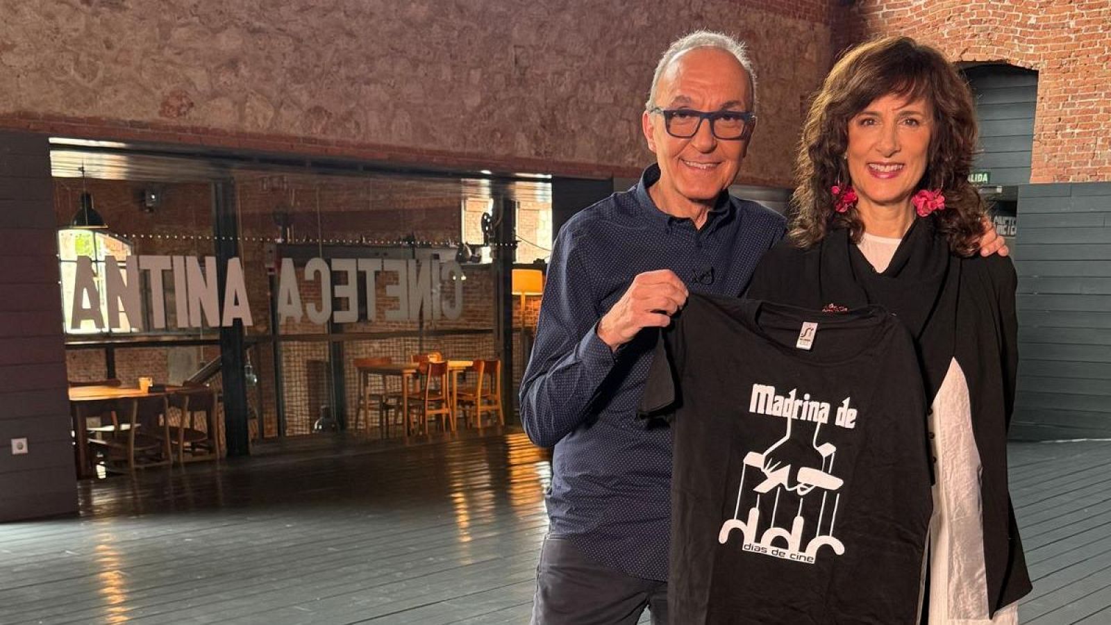 Gerardo Sánchez y Mariela Besuievski sonríen en una cineteca. Él muestra una camiseta con "Madrina de días de cine" y marionetas. Ella apoya su brazo en su espalda.