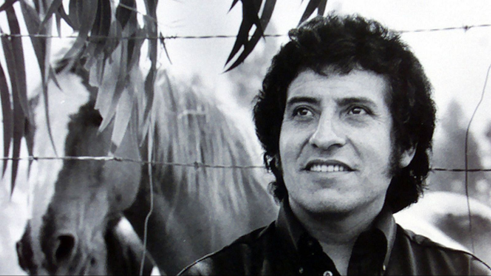 Primer plano de Víctor Jara, cantautor chileno, en blanco y negro. Mira hacia arriba con expresión serena y leve sonrisa. Fondo rural con hojas, alambre de púas y silueta de caballo.
