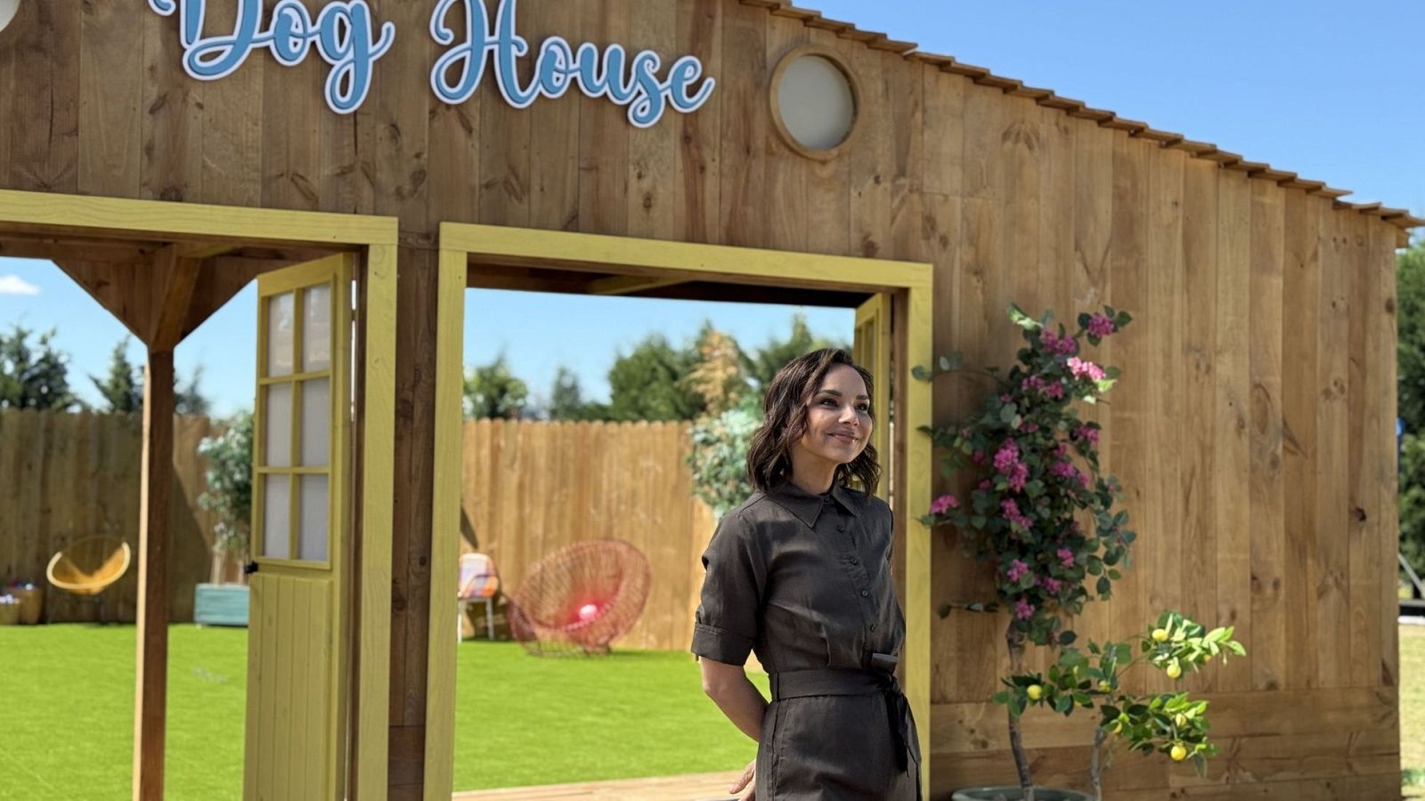 Chenoa, presentadora de 'Dog House', posa en un set de jardín con una estructura de madera y flores.