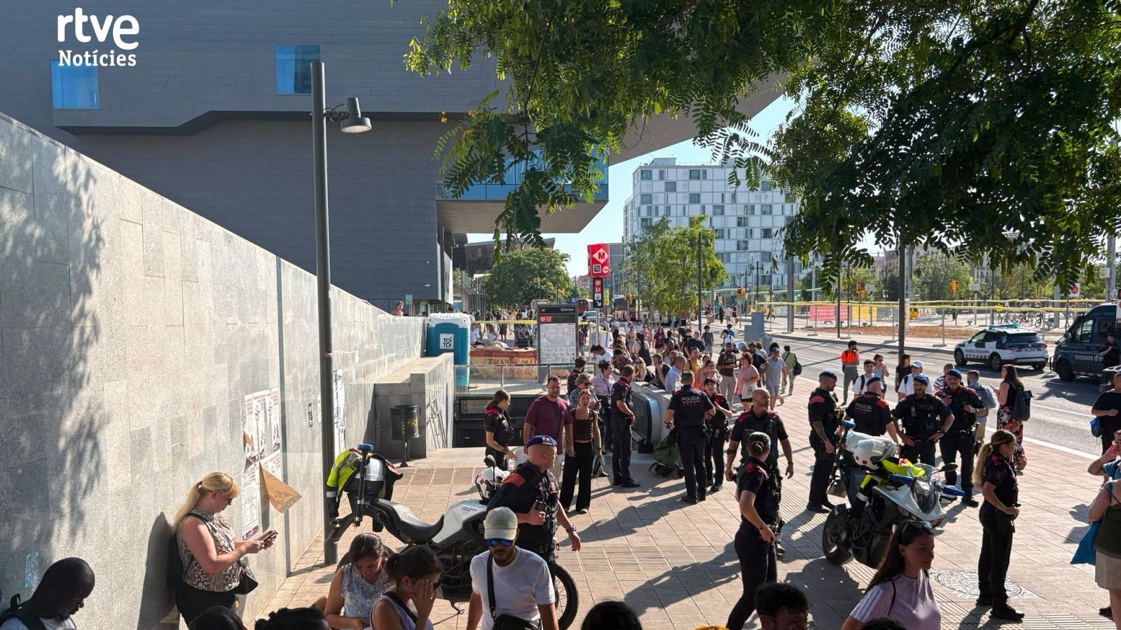 Multitud y policía en una calle urbana junto a una estación de metro, con el logo "rtve Noticias" visible. Se aprecian motocicletas policiales y un edificio moderno.