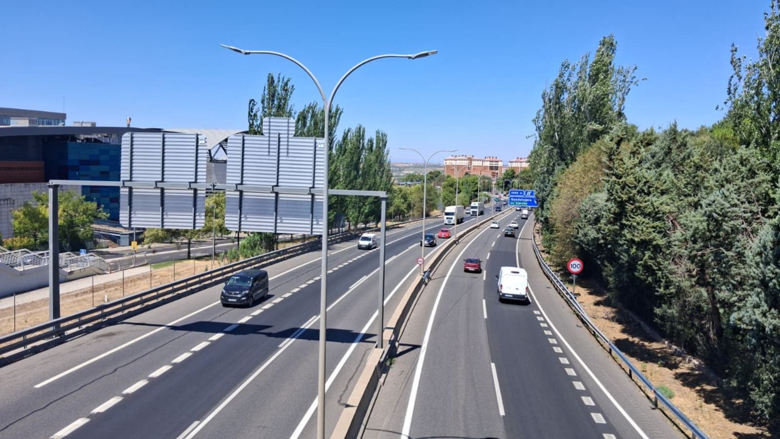Coches circulando por la A-2, en Guadalajara, antes de que comience la II Operación especial de tráfico del verano. El ambiente en la vía es tranquilo. Al fondo aparecen edificios y un cartel azul con indicaciones hacia la ciudad.