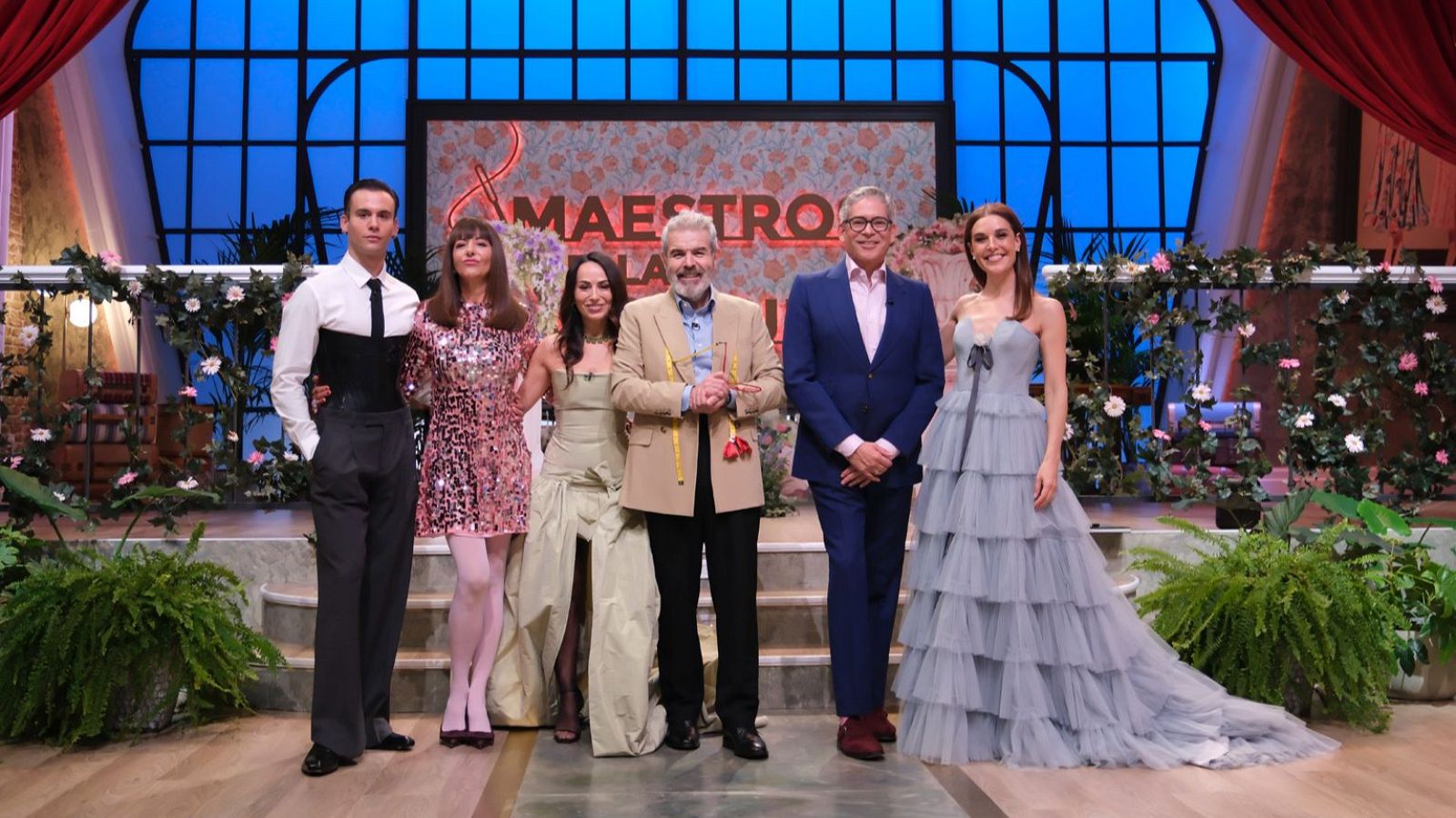 Seis personas posan en un escenario de "Maestros de la Costura" decorado con flores y el logo del programa. Se identifican a Palomo Spain, Raquel Sánchez Silva, María Escoté y Lorenzo Caprile.