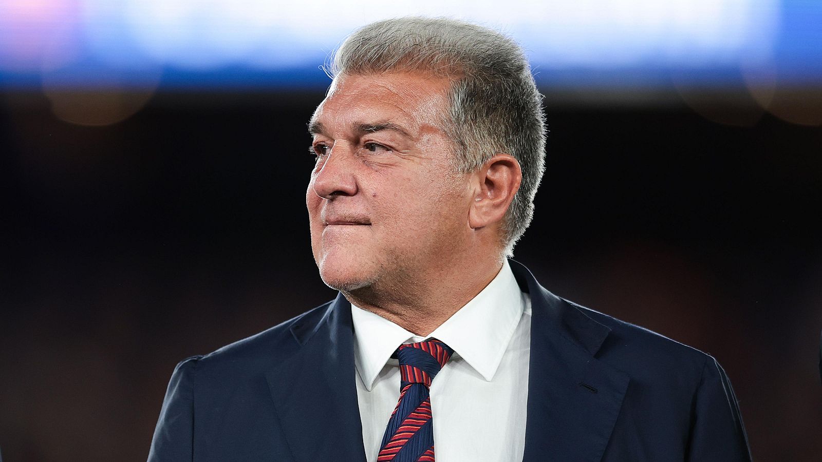 Joan Laporta, presidente del FC Barcelona, en un primer plano con traje y corbata, mirando hacia un lado con expresión seria. Fondo oscuro y desenfocado.