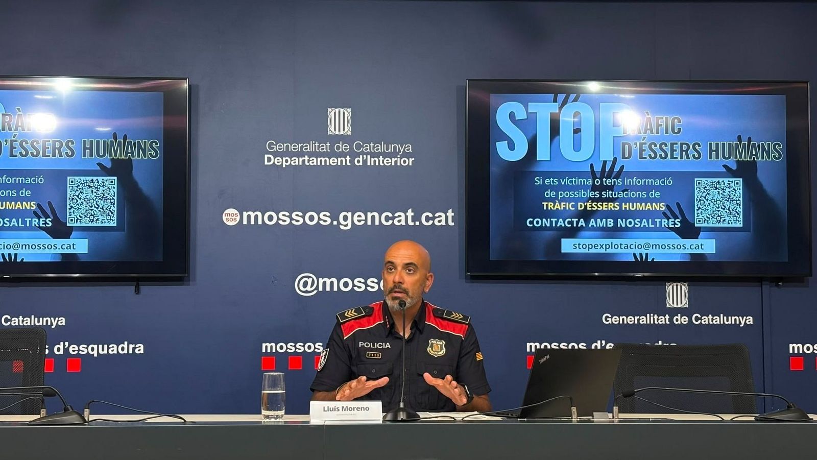 Subinspector Lluís Moreno de los Mossos d'Esquadra en rueda de prensa sobre tráfico de seres humanos. Pantallas con mensaje 'STOP TRÀFIC D'ÉSSERS HUMANS'.