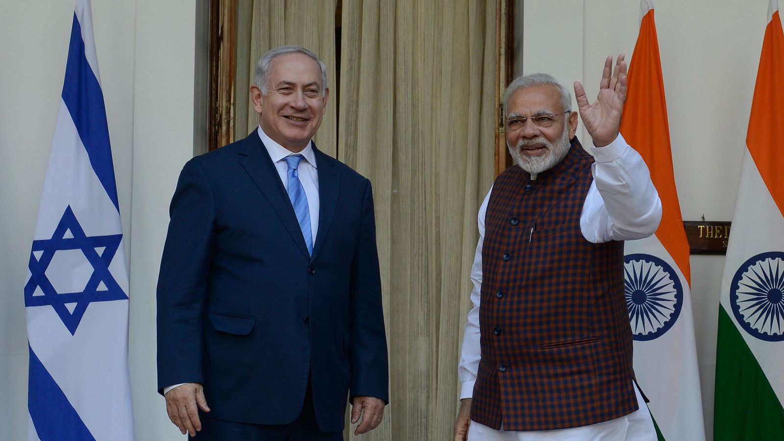 Benjamin Netanyahu y Narendra Modi, líderes de Israel e India, sonríen en un encuentro diplomático con las banderas nacionales de fondo.