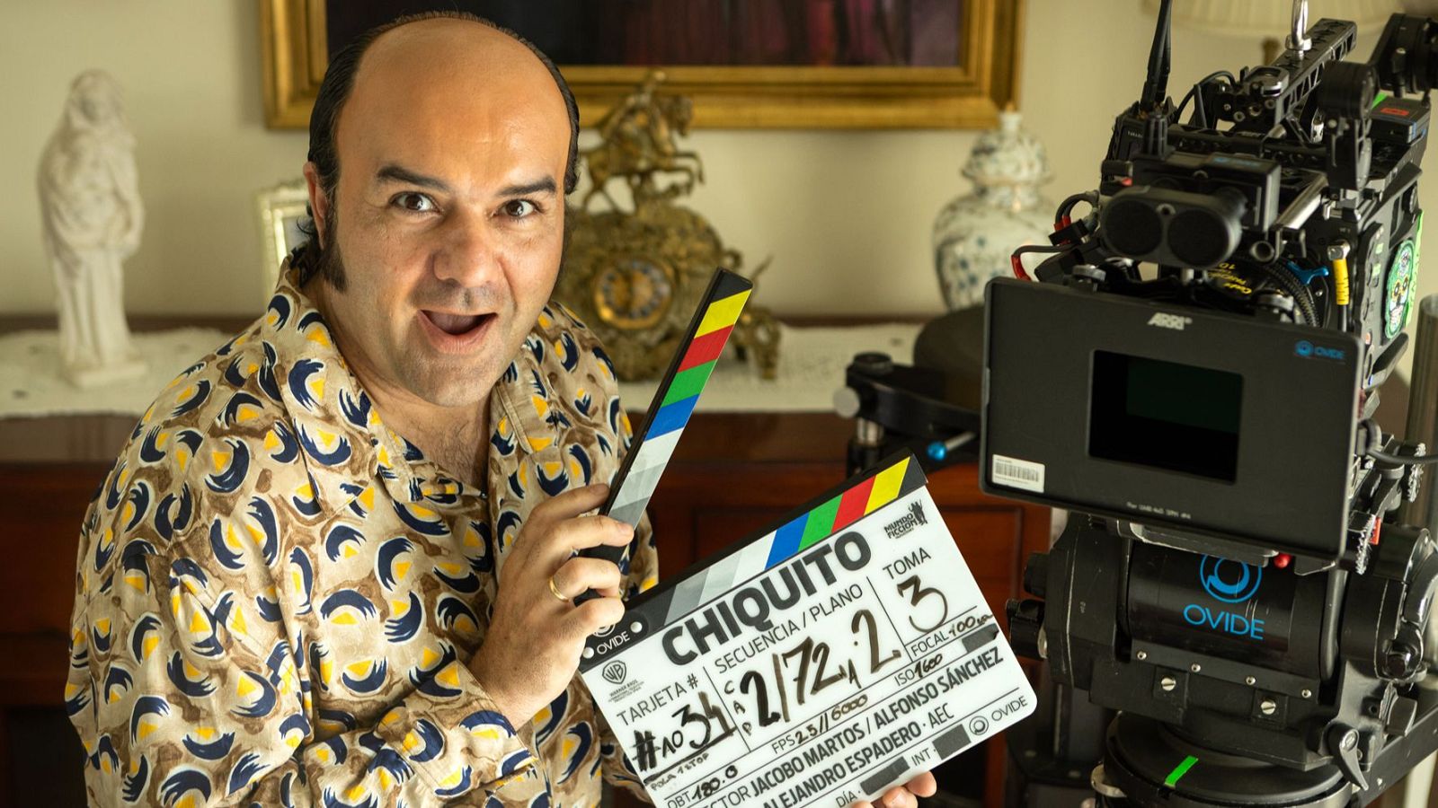 Alfonso Sánchez, actor y codirector, sostiene una claqueta de 'Chiquito el Grande' junto a una cámara Arri, en un set con decoración clásica.