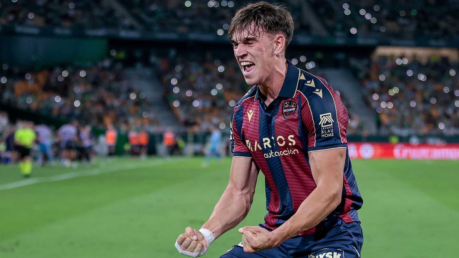 Carlos Espí, futbolista del Levante UD, celebra con euforia en un partido. Viste el uniforme granate y azul marino con "MARIOS" en el pecho.