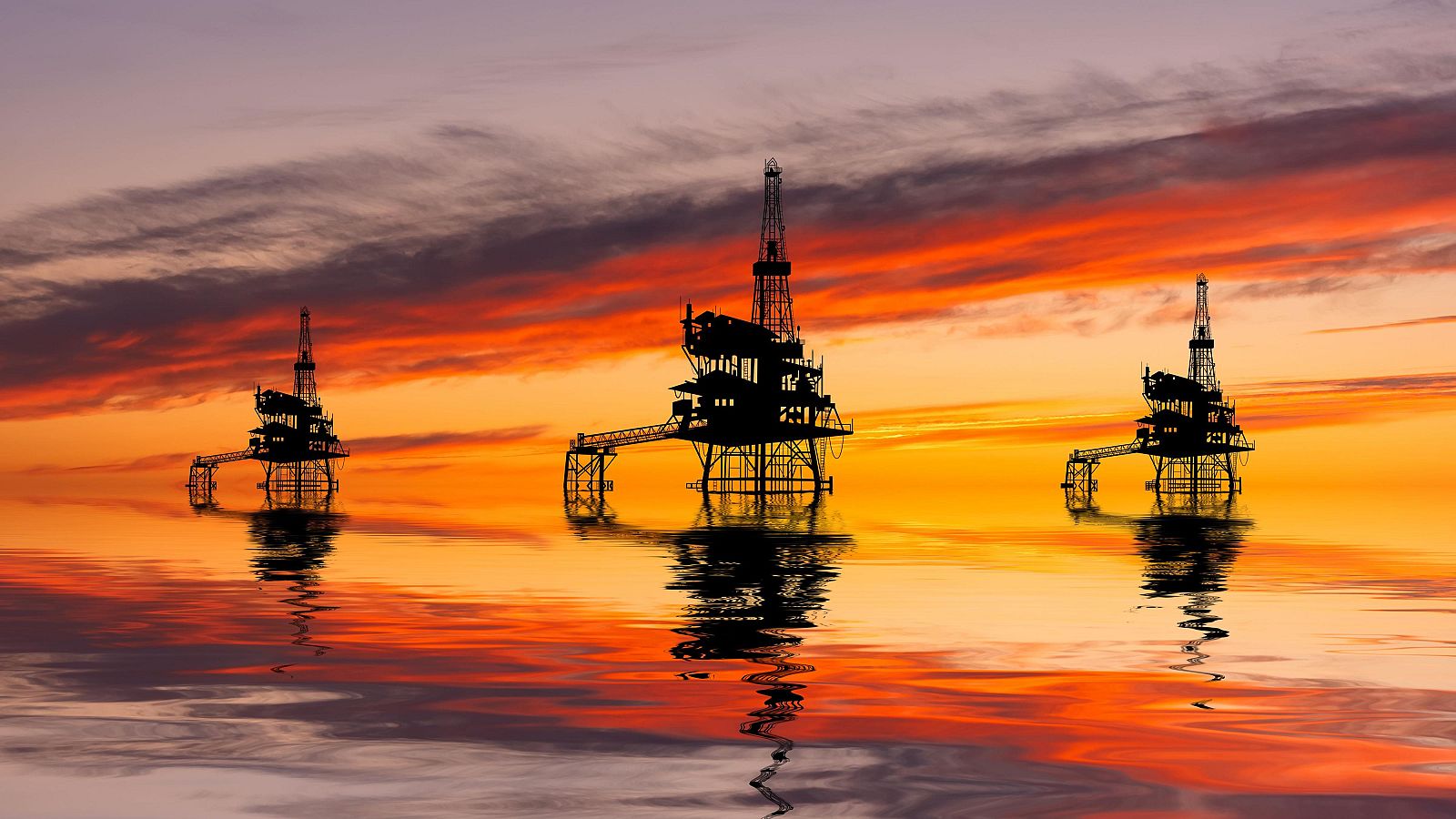 Tres plataformas petrolíferas se alzan como siluetas oscuras sobre un mar en calma que refleja un cielo anaranjado y rojizo, evocando la fuerza de la industria y la belleza natural.